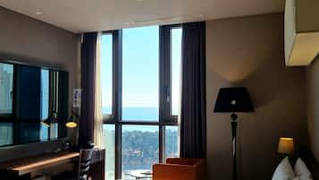 A hotel room with a bed, a desk, a chair, a TV, and a view of the city.