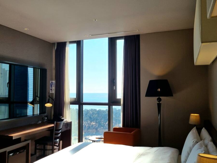 A hotel room with a bed, a desk, a chair, a TV, and a view of the city.