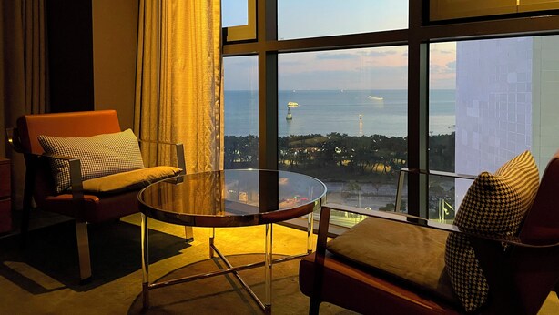 A modern hotel room with a large window offering a view of the sea and distant cityscape. - Best Louis Hamilton Hotel Haeundae (Busan)