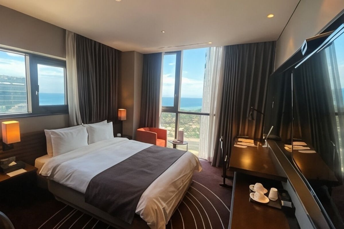 A hotel room with a large bed, two bedside tables, a TV, a small table, and a chair.