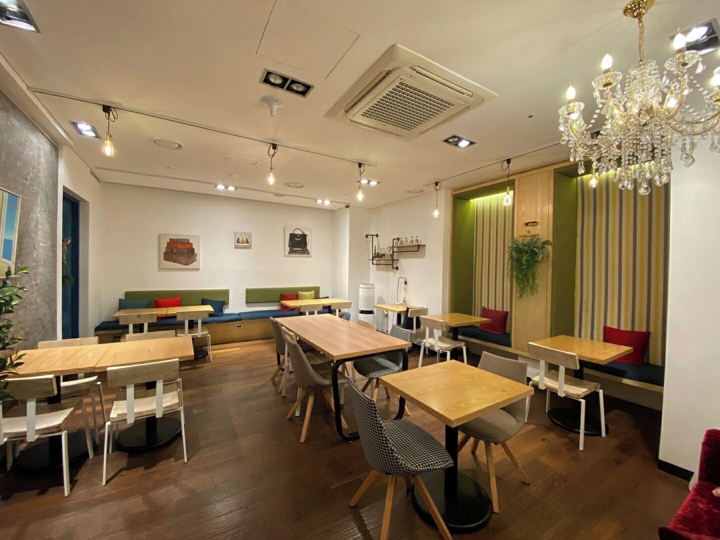 Ein modernes Café mit Holztischen und -stühlen, einer grünen gepolsterten Bank und einer Kristallleuchtre.