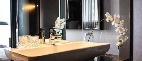 A modern bathroom with a large sink, two faucets, and three clear glasses on the counter.