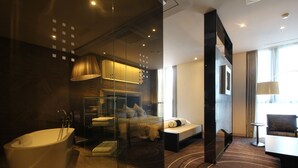 A modern hotel room with a large bathtub, a bed with a view, and a seating area with a table and chair. - Best Louis Hamilton Hotel Haeundae (Busan)