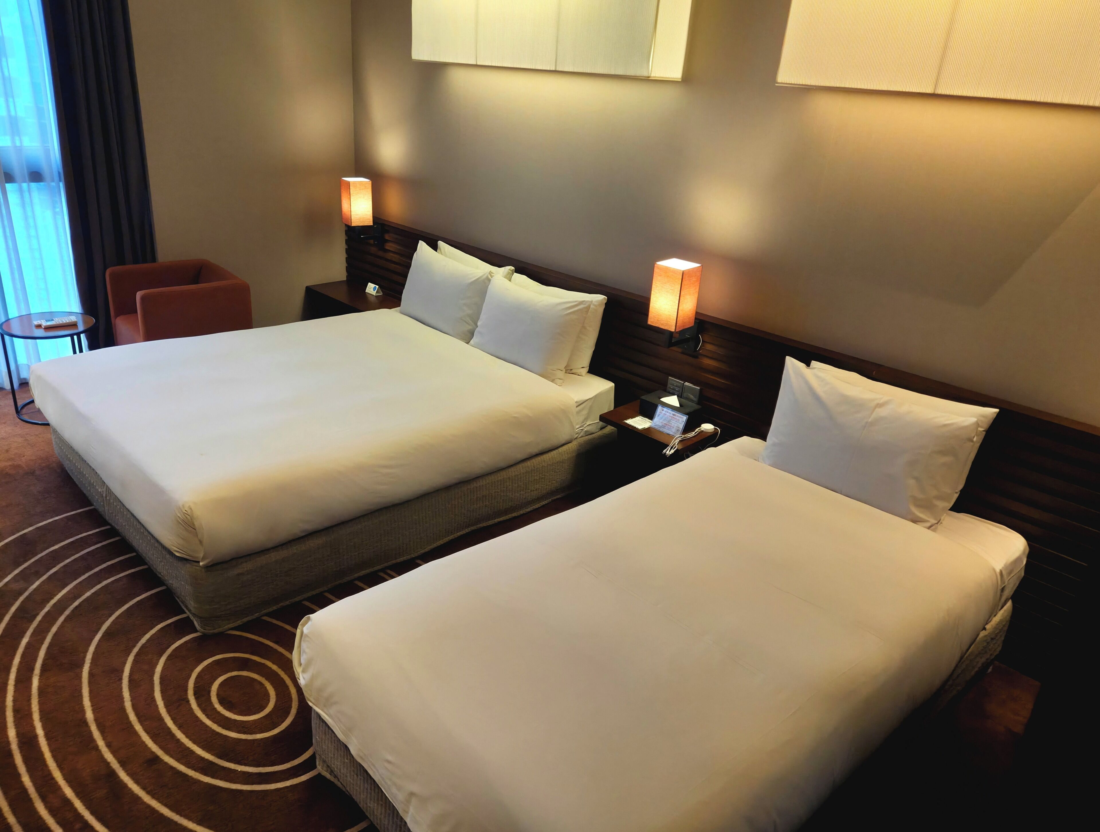 Ein Hotelzimmer mit zwei Betten, einem kleinen Tisch, einem Stuhl und einer Lampe.