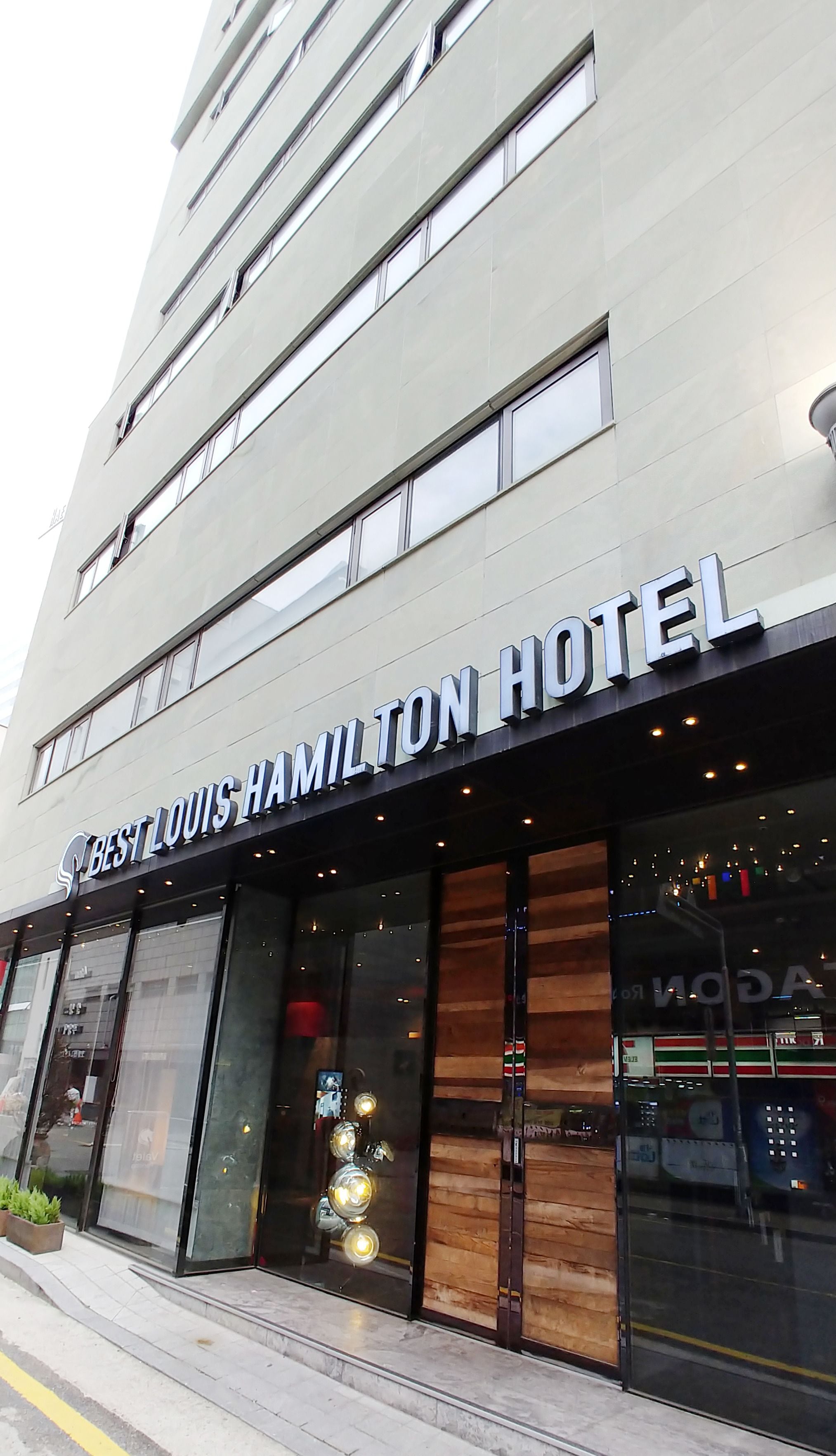 Das Best Louis Hamilton Hotel mit moderner Fassade, großen Fenstern und einer auffälligen Schrifttafel über dem Eingang.
