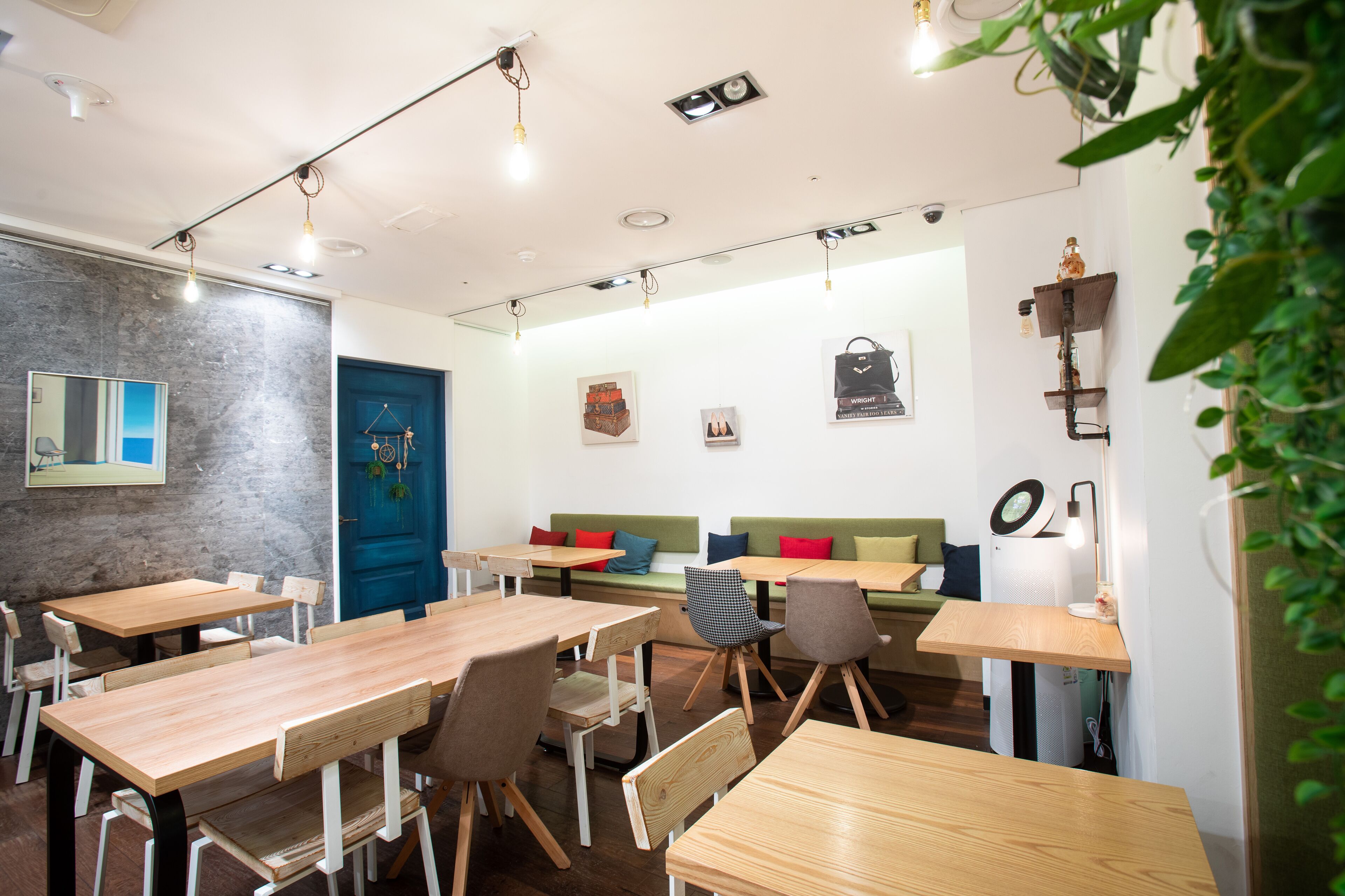 A modern cafe with wooden tables and chairs, a blue door, and a green sofa.