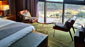 A hotel room with a large bed, a seating area with a table, and a view of the sea and cityscape through large windows. - Best Louis Hamilton Hotel Haeundae (Busan)