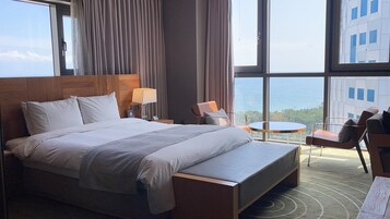 Una habitación de hotel moderna con una cama grande, un área de estar con una mesa y sillas, y vista al océano.