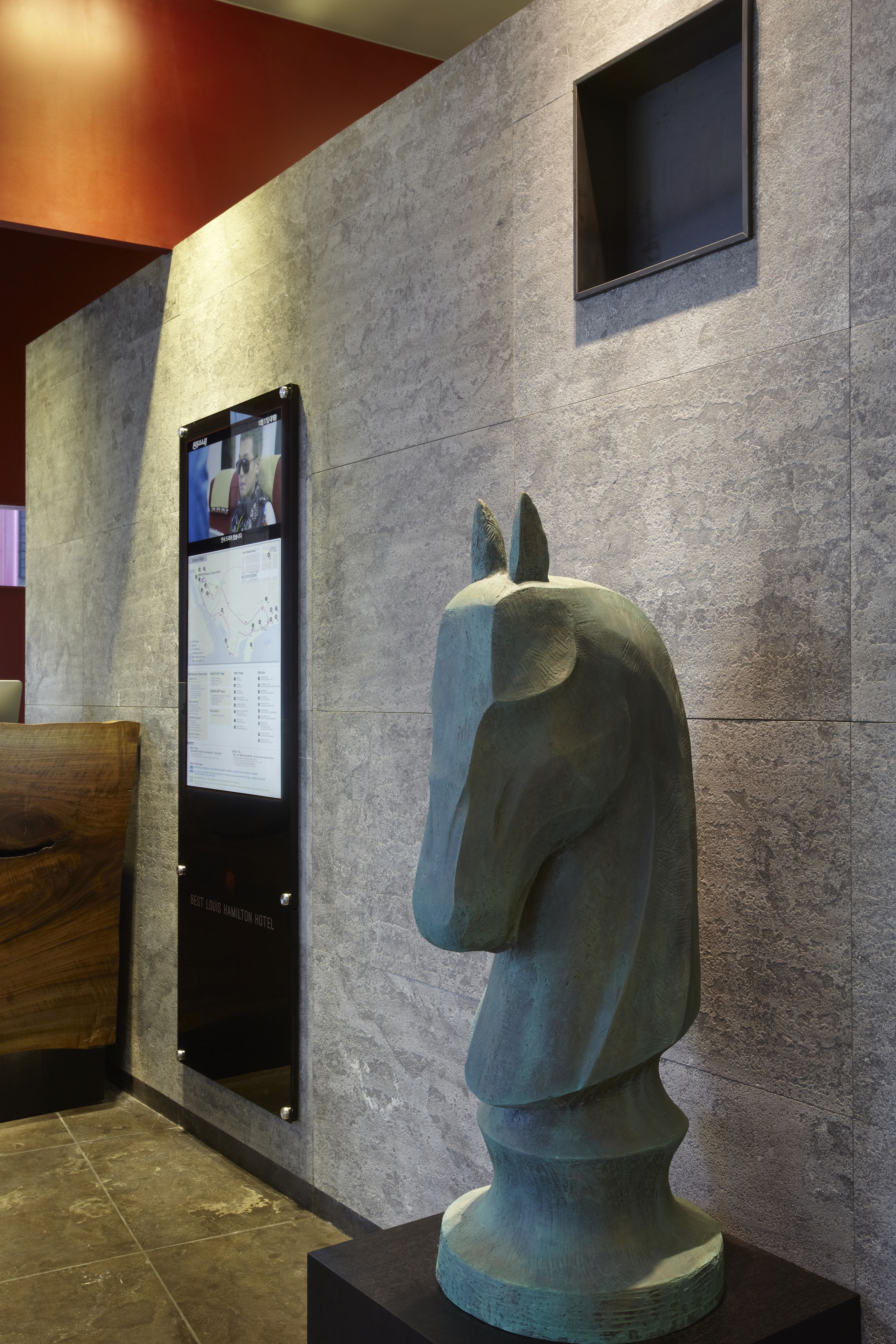 Una estatua de un caballo sobre un pedestal, un panel de información digital y un banco de madera.