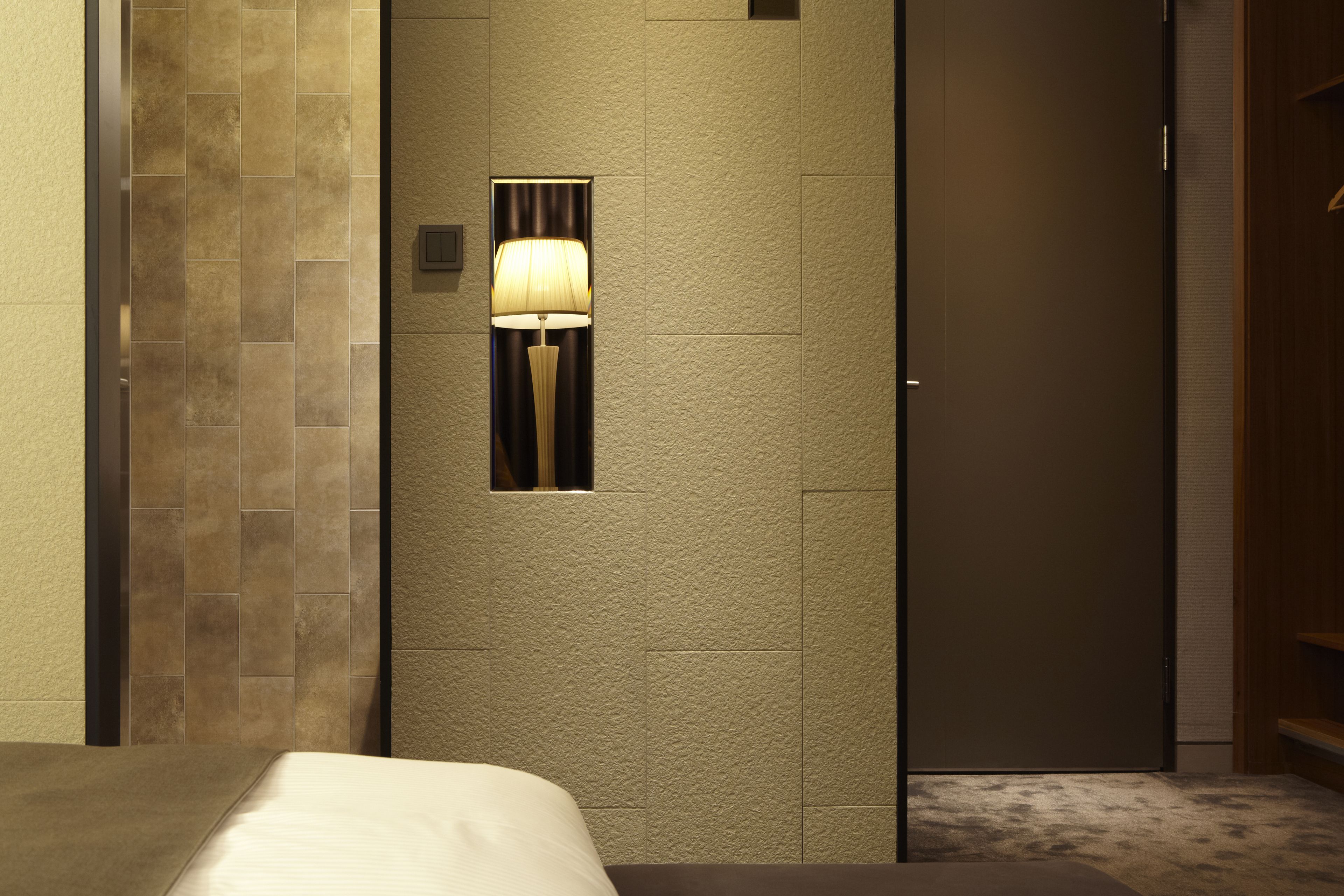 Una habitación de hotel con cama, lámpara de pared y una puerta.