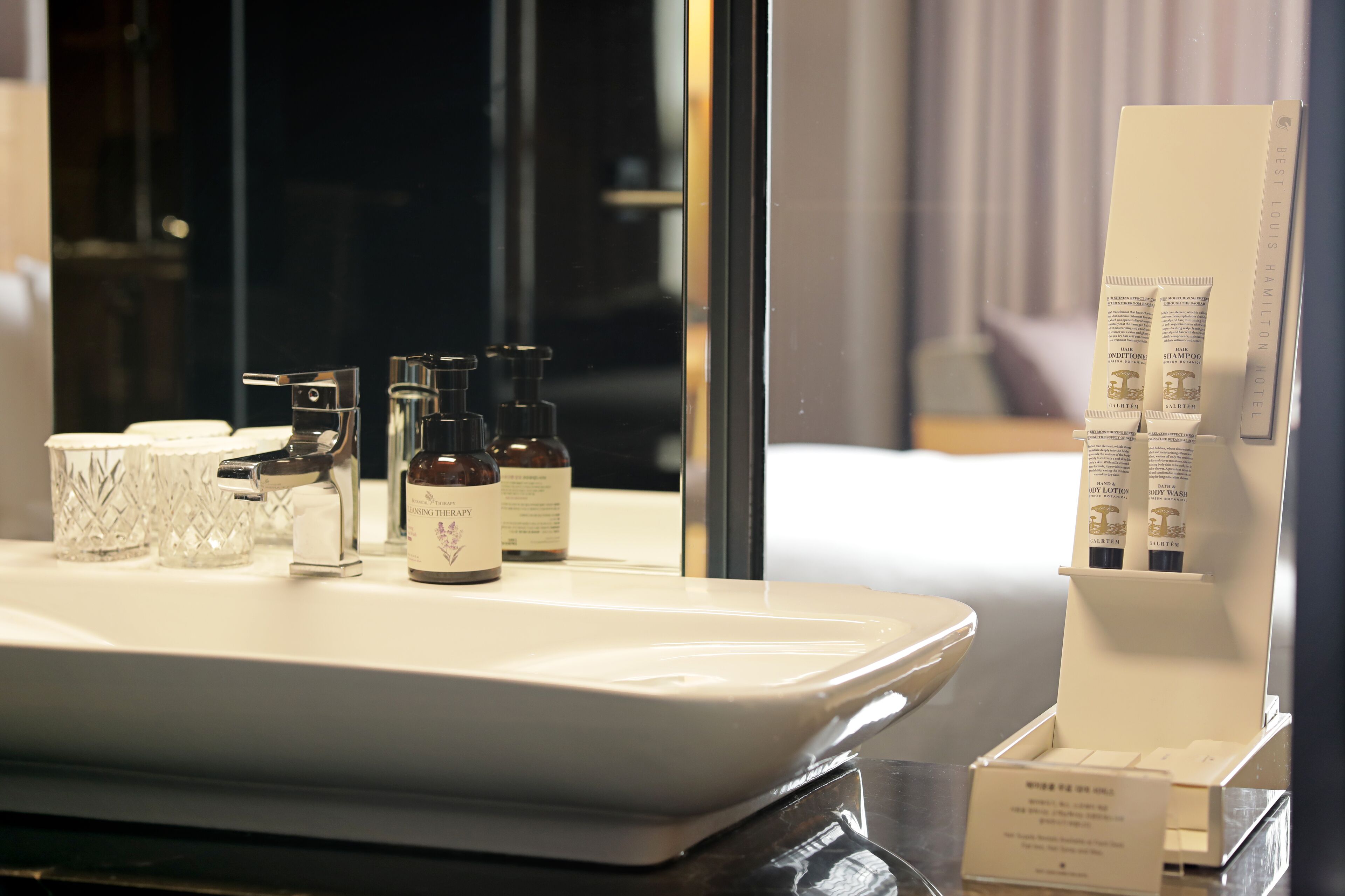 A hotel bathroom with a large sink, toiletries, and a mirror.