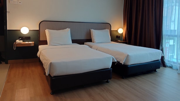 A hotel room with two beds, a bedside table with a phone, a wall-mounted light, and a window with curtains. - K Hotel (Kuala Lumpur)