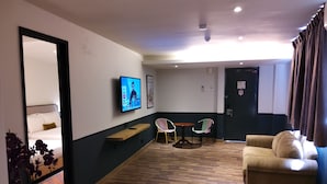 A hotel room with a bed, a TV mounted on the wall, a wooden table, two chairs, a sofa, and a large mirror. - K Hotel (Kuala Lumpur)