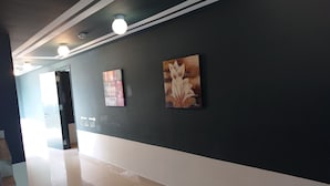 A hallway with a dark wall, three ceiling lights, and two artworks. - K Hotel (Kuala Lumpur)