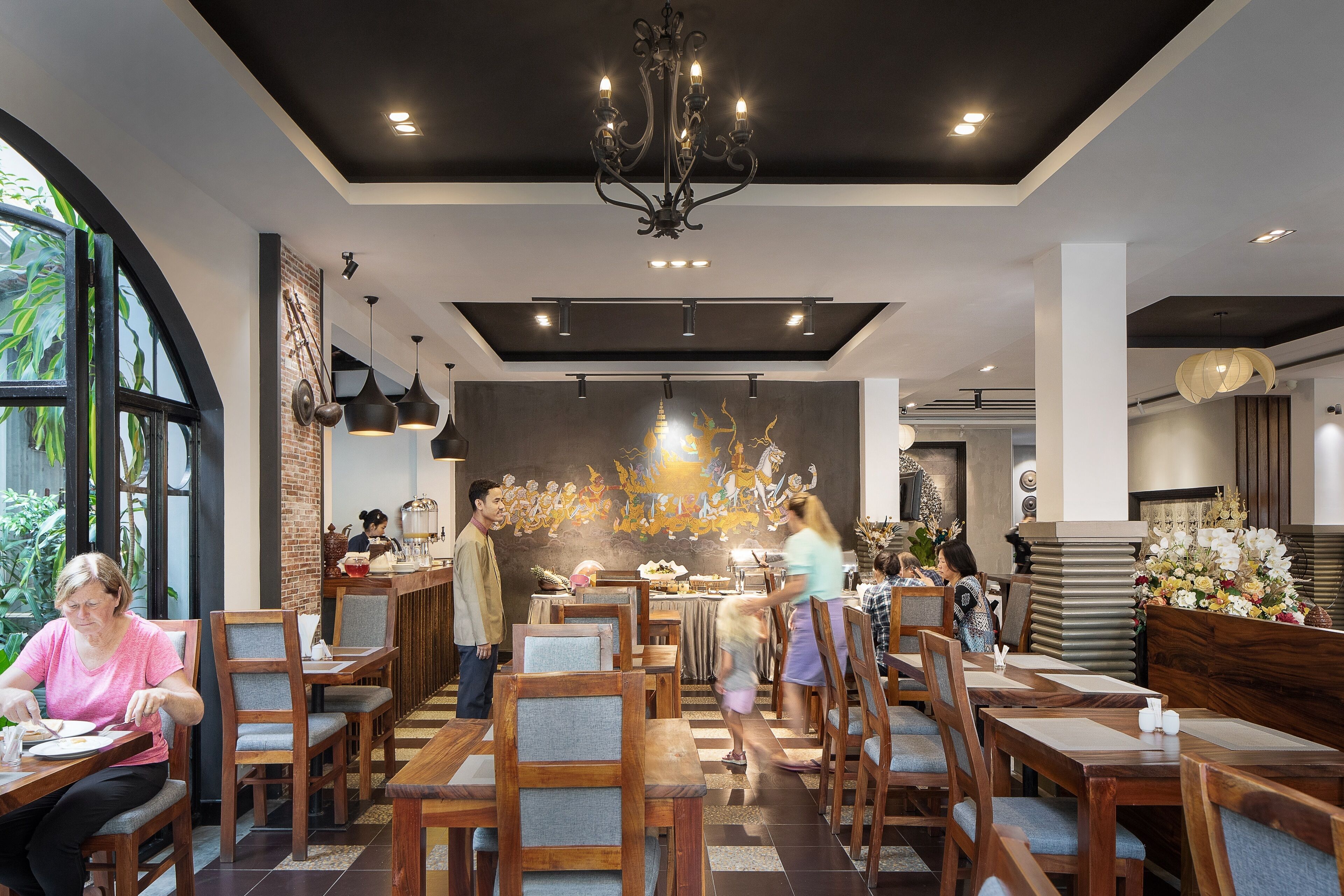 Um restaurante com mesas e cadeiras de madeira, um candelabro e um mural na parede.
