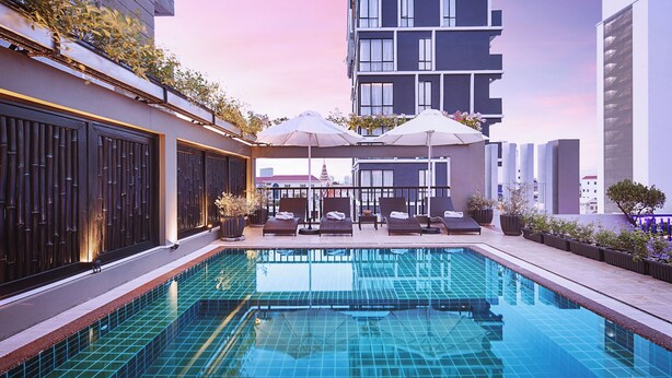Ein Dachpool mit Liegestühlen und Sonnenschirmen, umgeben von modernen Gebäuden.