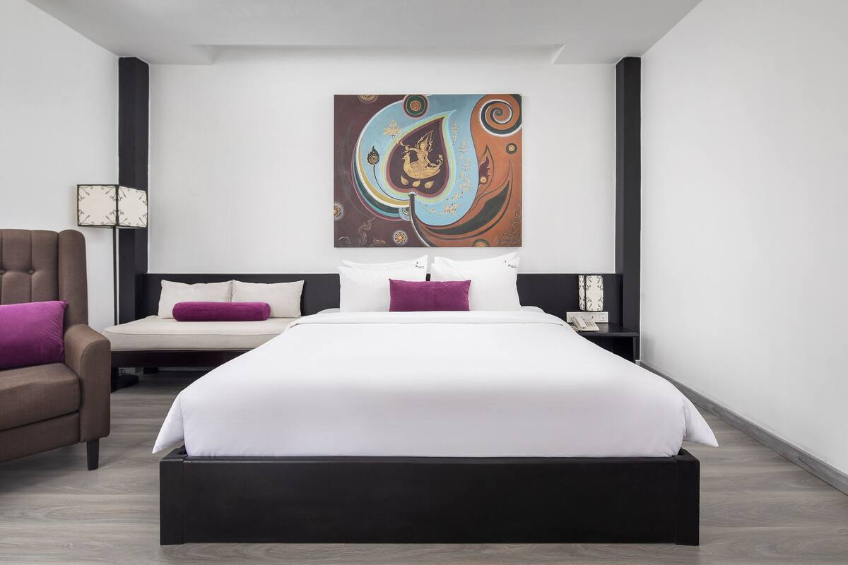 Ein modernes Hotelzimmer mit einem großen Bett, einer Couch, einem Nachttisch und einem an der Wand befestigten Kunstwerk.