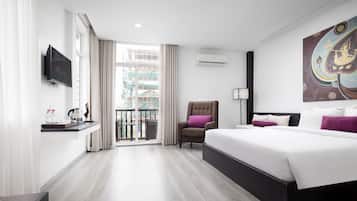 Una habitación de hotel moderna con una cama grande, un televisor de pantalla plana en la pared, una silla con un cojín morado y un balcón con vistas a la ciudad.