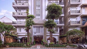 Ein mehrstöckiges Hotel mit Balkonen, einem zentralen vertikalen Gestaltungselement und einem gepflegten Garten mit Bäumen und Pflanzen.