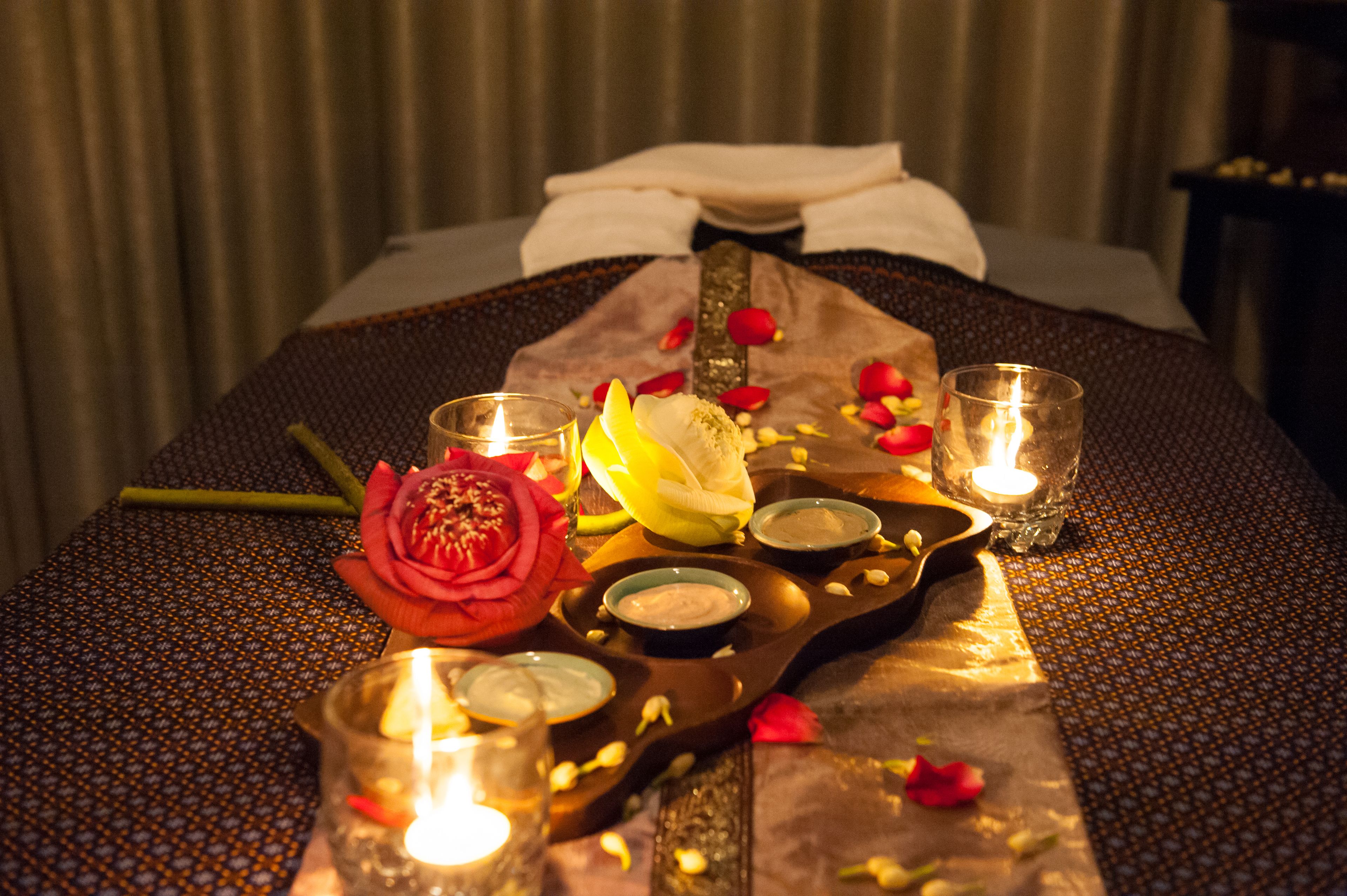 A neatly arranged bed with rose petals, candles, and a tray of snacks.