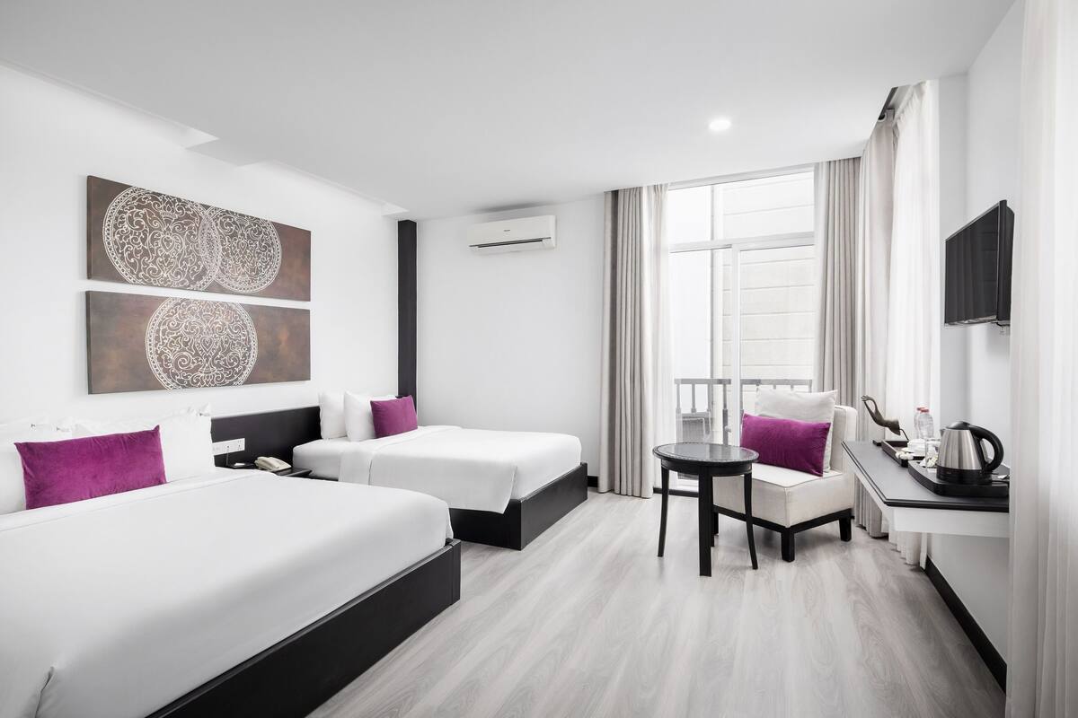 Ein modernes Hotelzimmer mit zwei Betten, einem kleinen Tisch, einem Stuhl, einem Fernseher und einem Fenster mit Vorhängen.