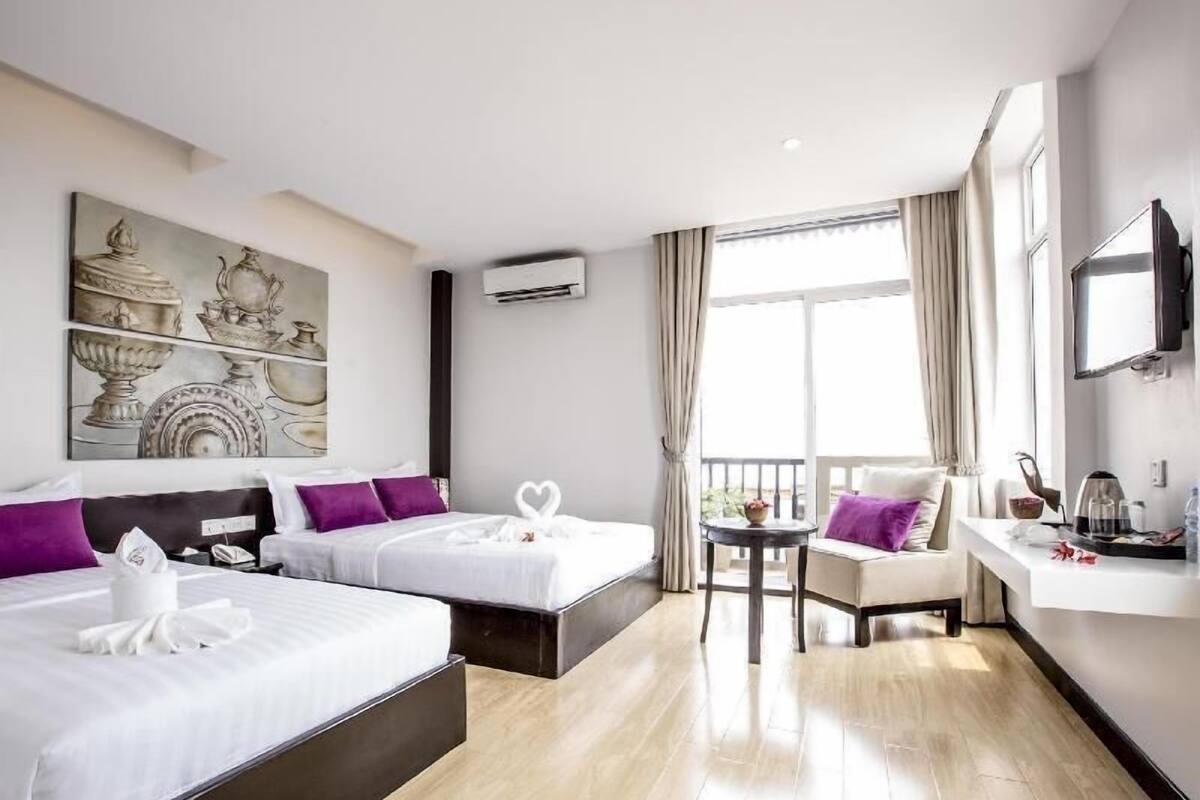 Ein Hotelzimmer mit zwei Betten, einem Schreibtisch, einem Fernseher und einem Balkon.