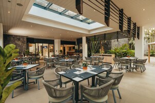 A spacious indoor dining area with multiple tables and chairs, a stone wall, and a view of the outdoors.