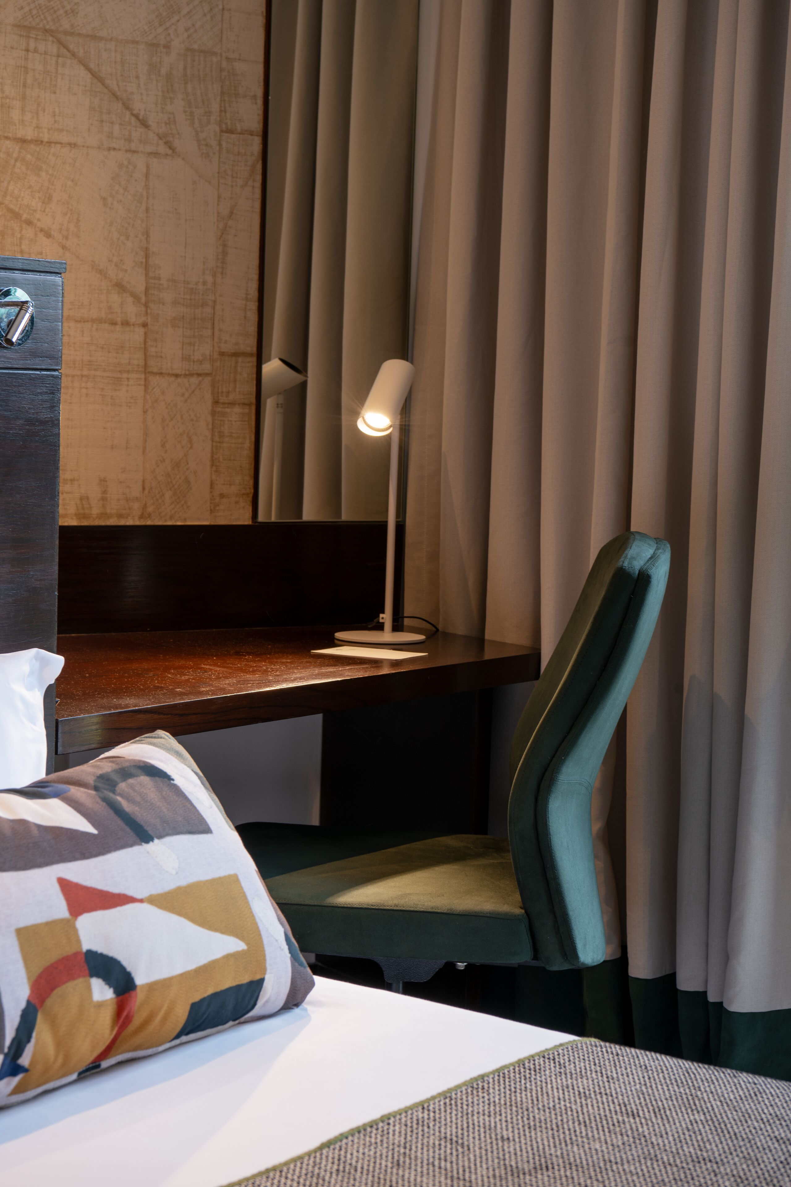 A hotel room with a bed, a desk, a chair, a lamp, and a large window with curtains.