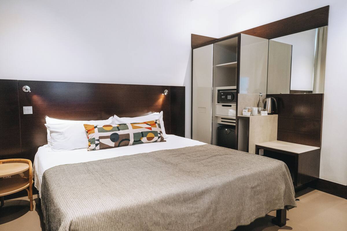 Une chambre d’hôtel comprenant un lit, une table de chevet, une chaise, un miroir et une armoire.