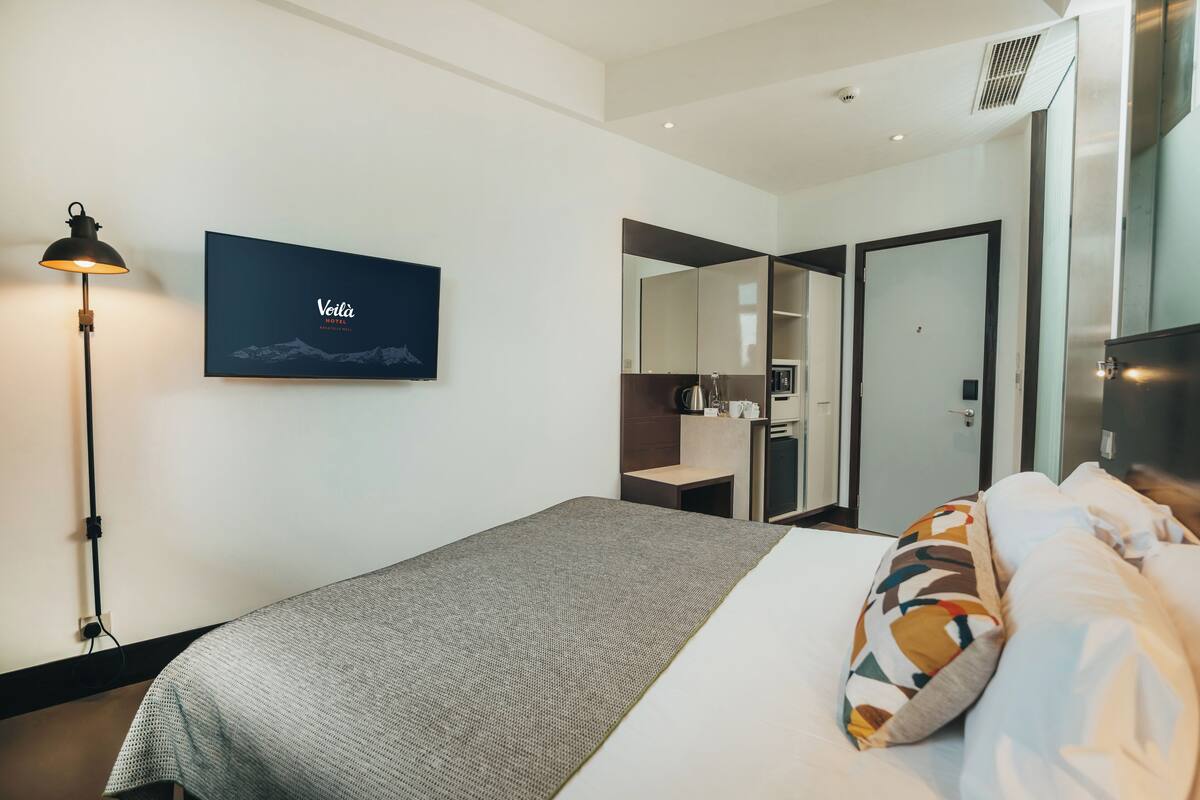 Une chambre d’hôtel moderne équipée d’un lit, d’un bureau, d’un miroir et d’une œuvre d’art encadrée au mur.