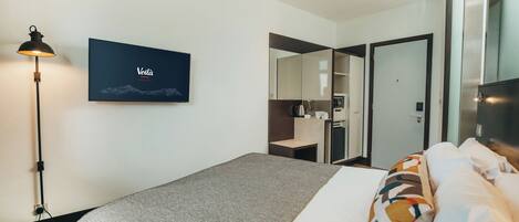 A modern hotel room with a bed, a desk, a mirror, and a framed artwork on the wall.
