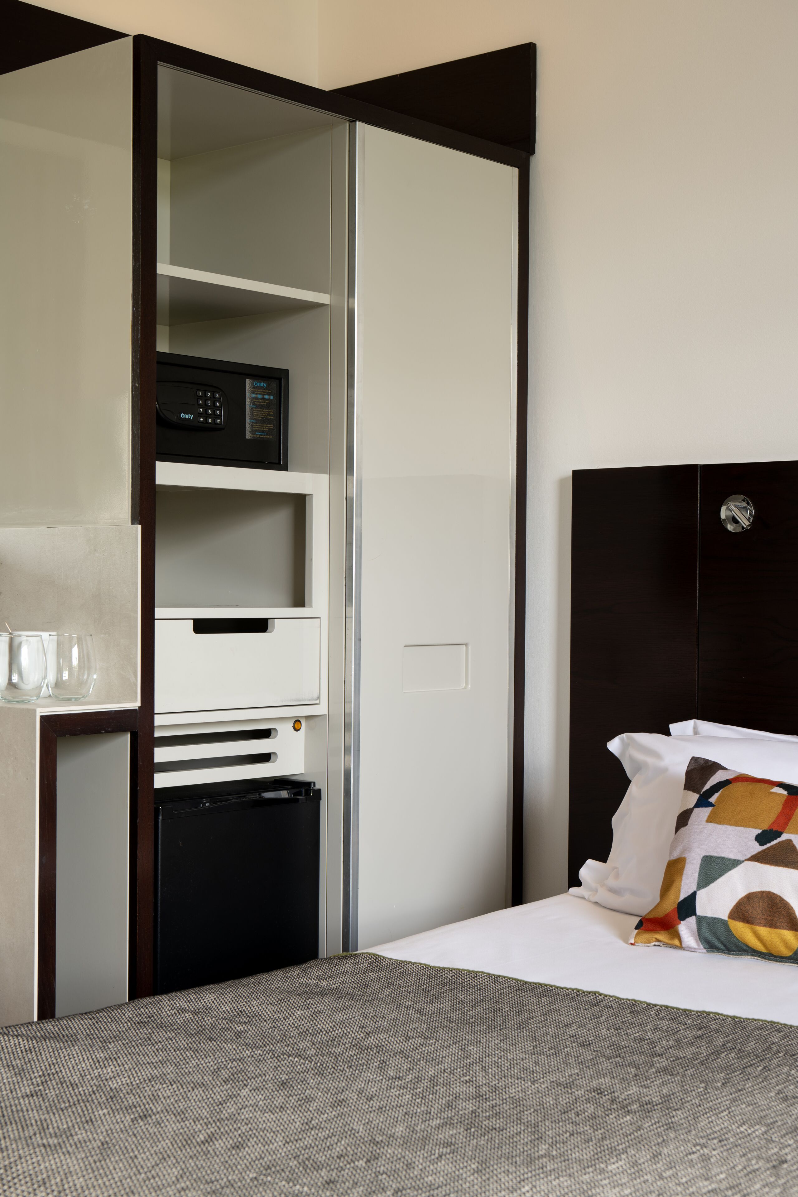 Habitación de hotel con cama, armario, microondas y un pequeño electrodoméstico negro.