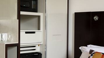 A hotel room with a bed, a wardrobe, a microwave, and a small black appliance.