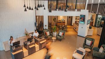 A modern hotel lobby with a reception desk, seating area, and a staircase leading to an upper level.