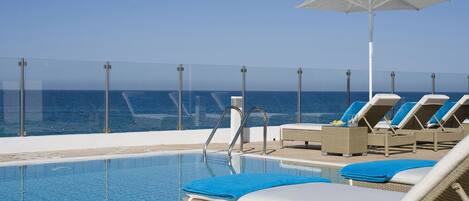 A poolside area with lounge chairs and a large umbrella, overlooking a body of water.