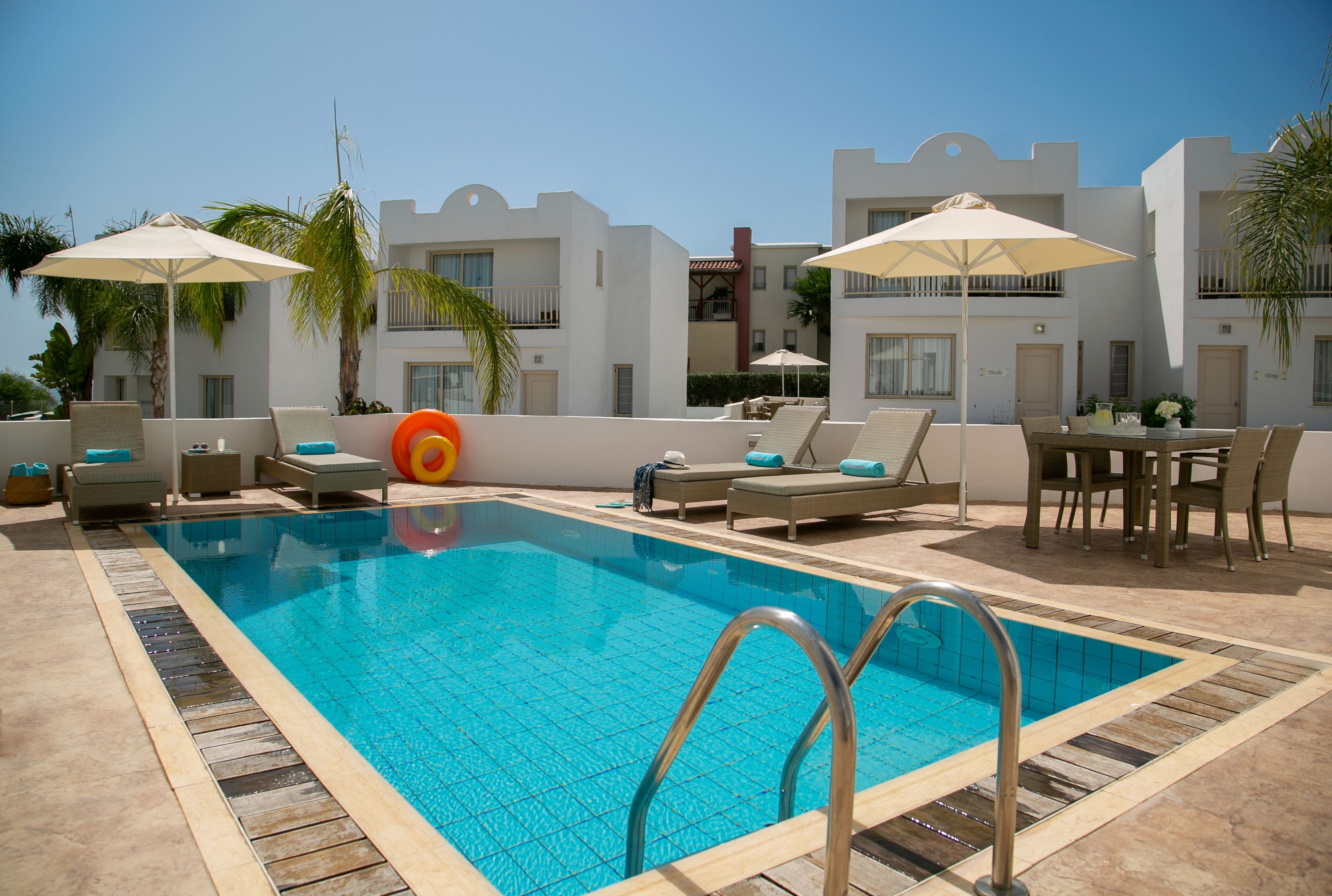 A swimming pool with lounge chairs and umbrellas, surrounded by white buildings with balconies.