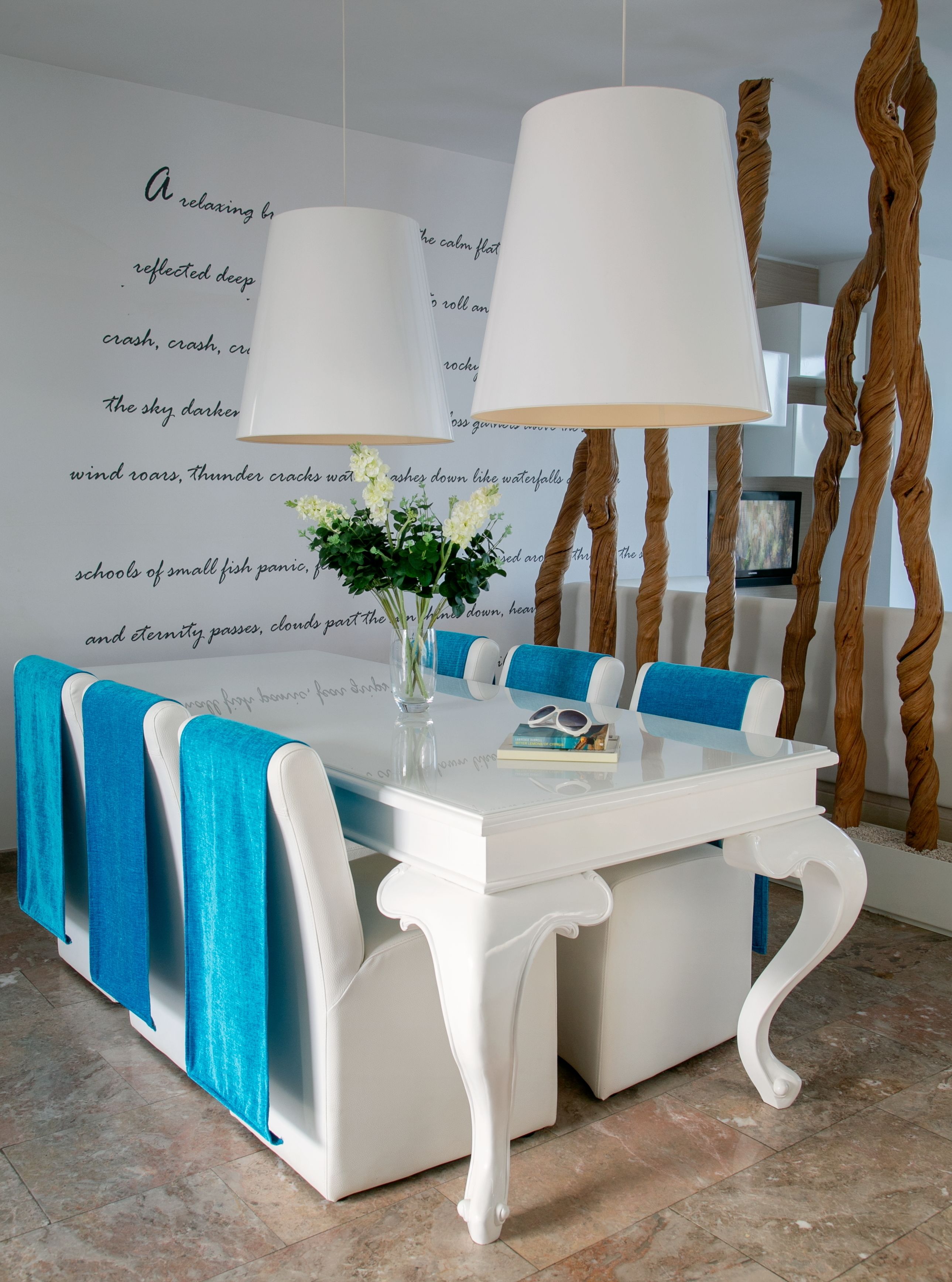 A dining area with a white table, blue chairs, and a vase with flowers.