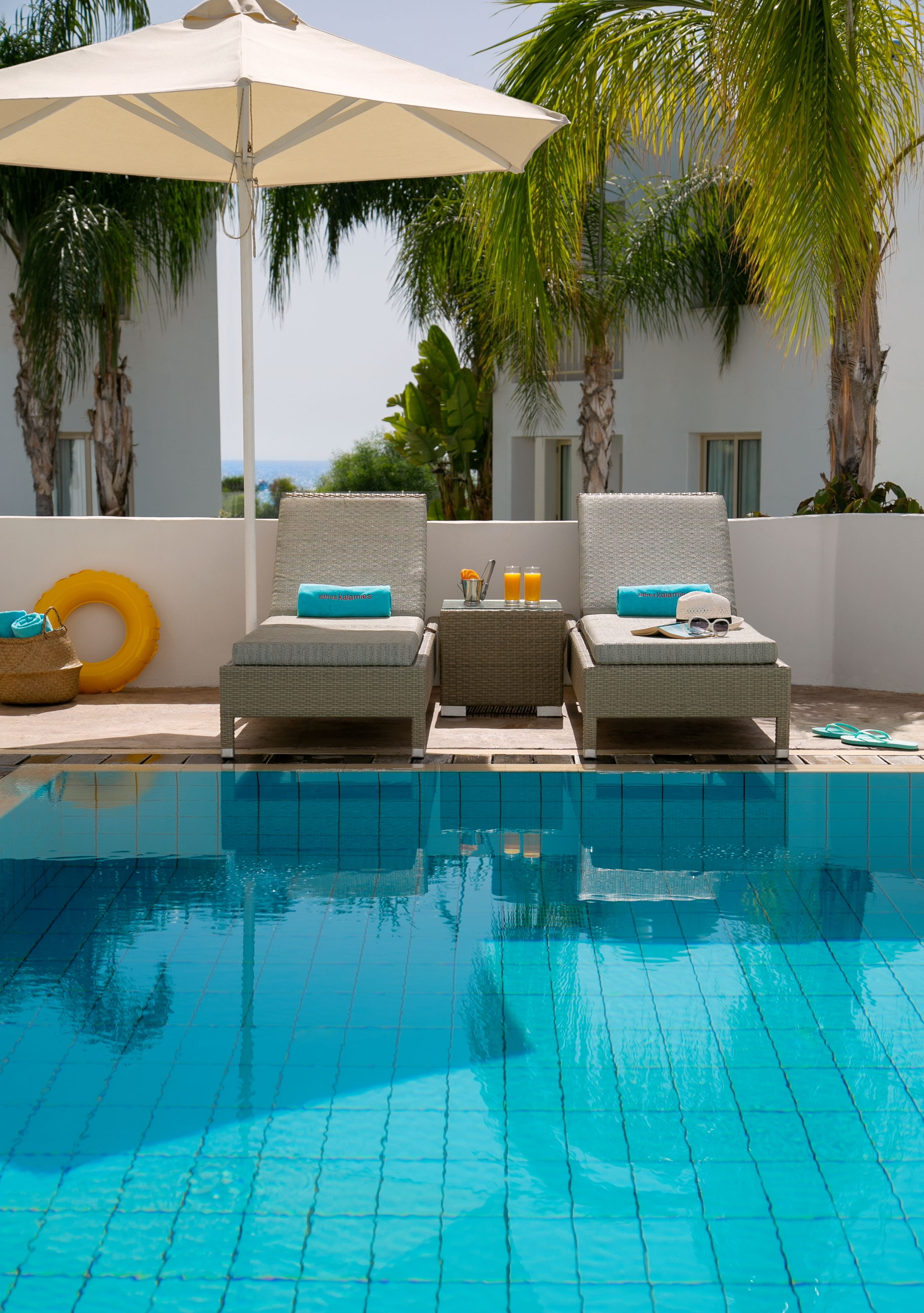 A poolside area with two wicker lounge chairs, a yellow inflatable ring, and a white umbrella.