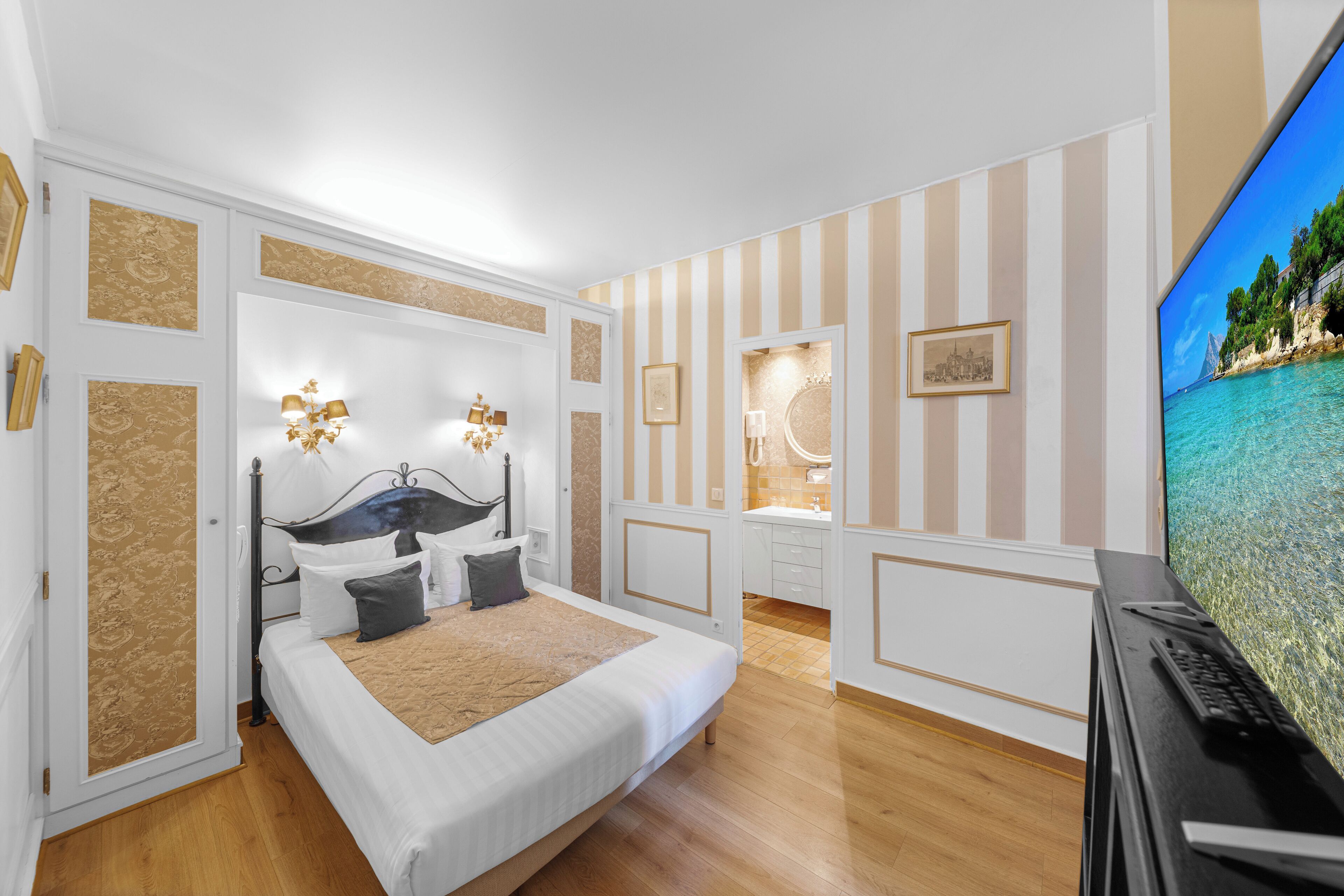 Een slaapkamer met een bed, nachtkastjes, een televisie en een badkamer met een spiegel en wastafel.