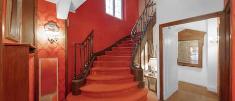 A spiral staircase with red carpeted steps and wooden railings, leading to a landing with a wooden door and a map on the wall.