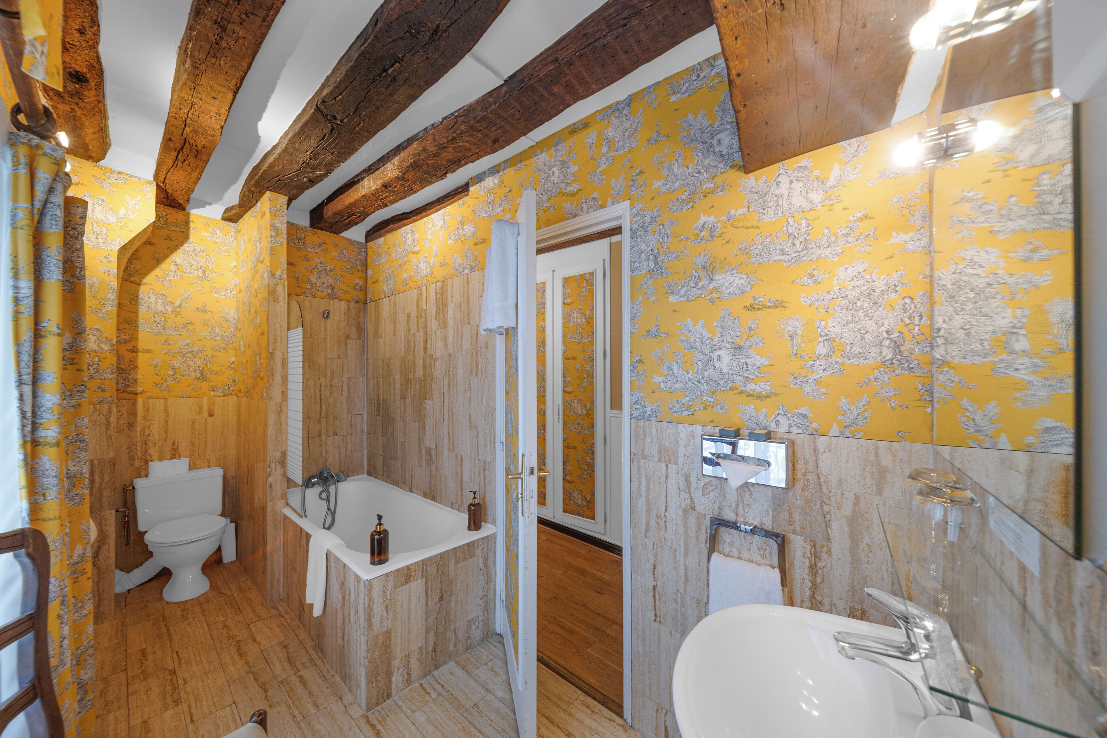 A bathroom with wooden beams, a toilet, a bathtub, and a sink.
