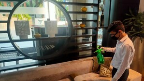 Une personne se tient près d’un canapé, devant un miroir rond et des étagères, dans un intérieur moderne.