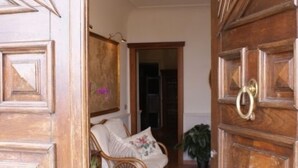 Una puerta de madera con picaporte de latón, un sofá de mimbre con cojines, una alfombra estampada y una planta en maceta.