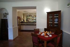 Zona pranzo con tavolo apparecchiato per la colazione, un bancone al bar sullo sfondo e un mobile con ante in vetro.