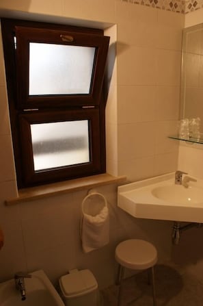 Un bagno con finestra, lavandino, water e un piccolo sgabello.