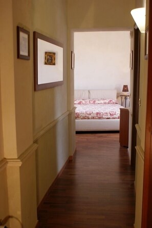 Un pasillo estrecho con suelo de madera que lleva a un dormitorio con cama y mesita de noche.