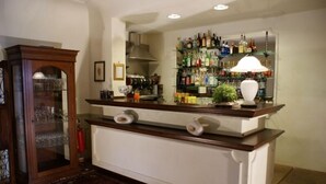 Una zona de bar con mostrador de madera, estanterías llenas de botellas de licor y una lámpara decorativa.