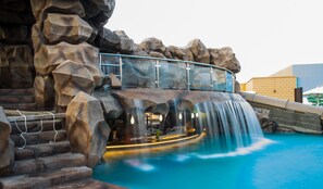 A pool area with a waterfall, a glass bridge, and a bar area. - Royal Residence Hotel & Spa (Umm al Quwain)