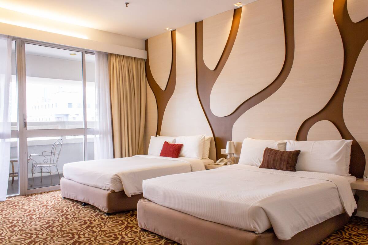 A hotel room with two beds, a large window with curtains, and a patterned carpet.