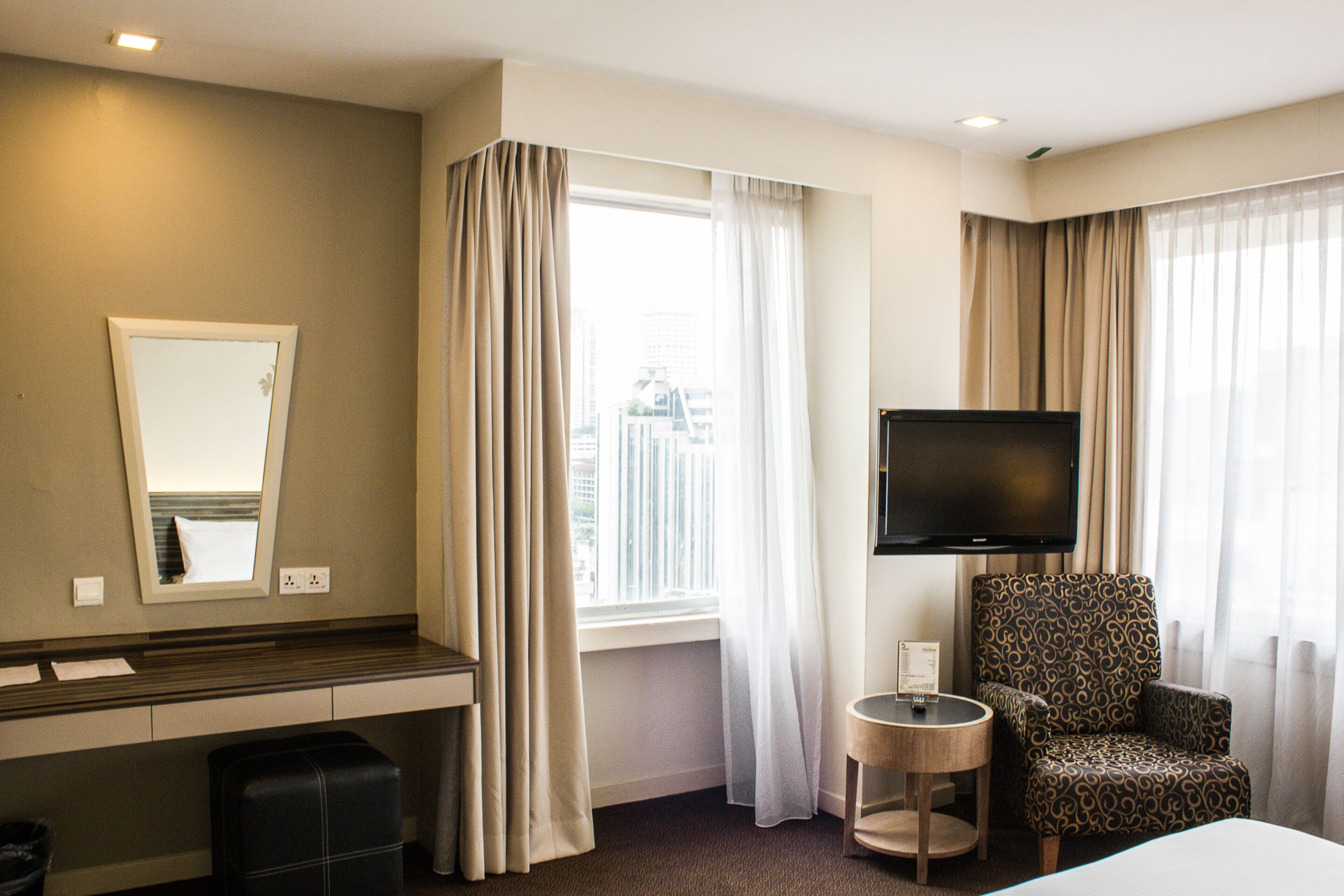 A hotel room with a bed, a television, a chair, a small table, and a window with curtains.